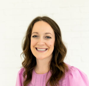 A women smiling in a pink shirt and curled brown hair