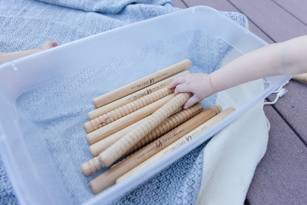 Hand of child grabbing rhythm sticks out of a bin